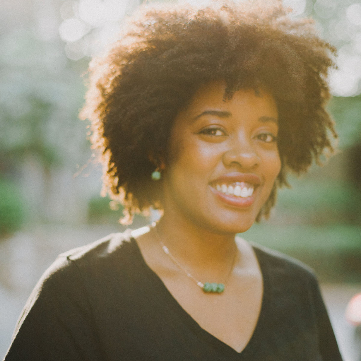 Smiling woman with natural afro hairstyle and green jewelry outdoors in soft sunlight