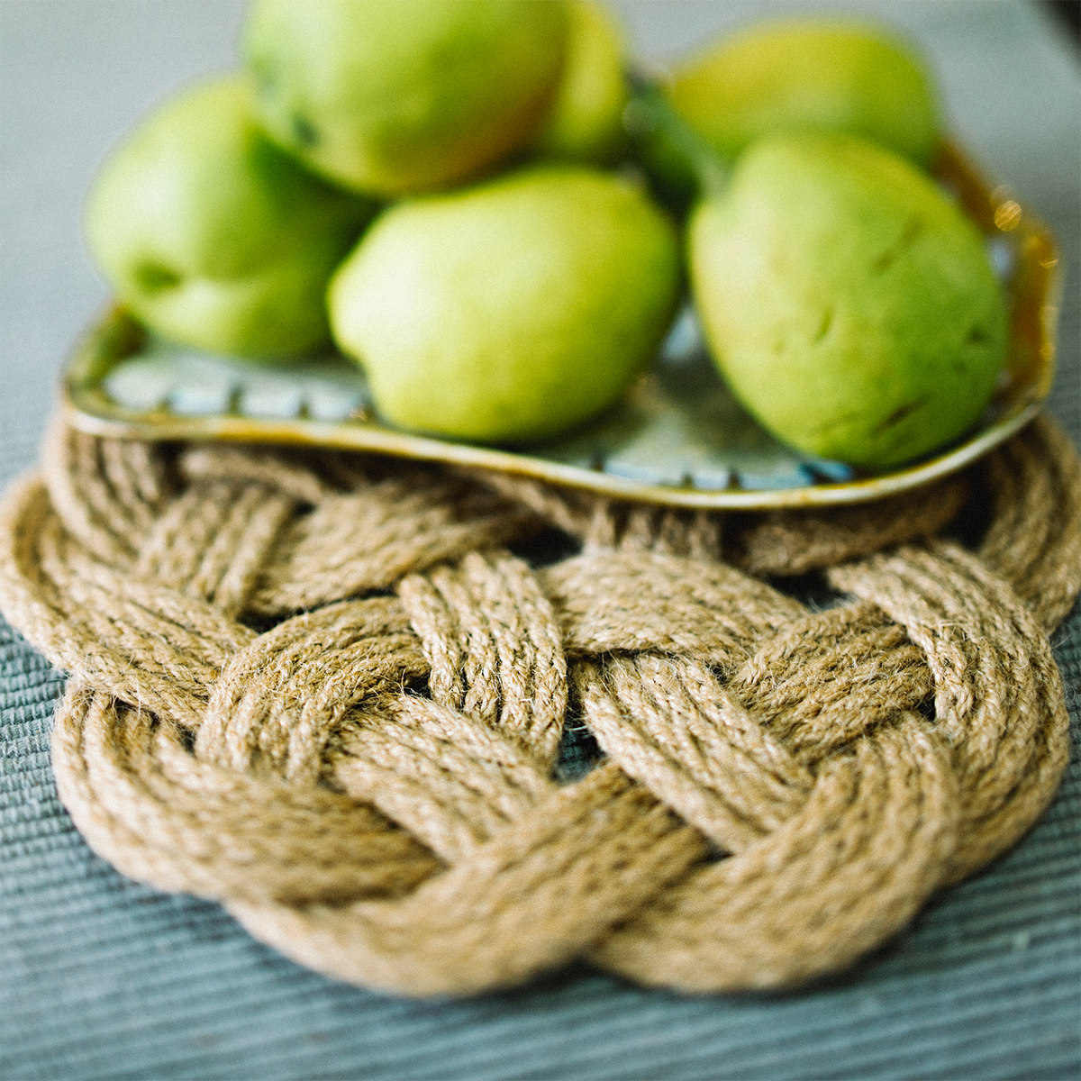 Woven rope trivet under a plate of green pears on a textured surface