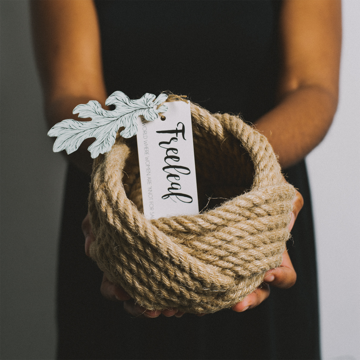 Person holding a handcrafted rope basket with a Freeleaf tag and decorative leaf accent