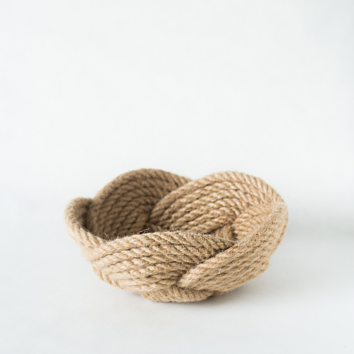 Woven natural rope bowl on a white background, decorative storage accessory.