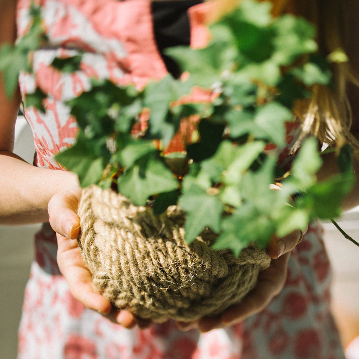 Woman holding a green potted ivy plant in a woven rope basket outdoors