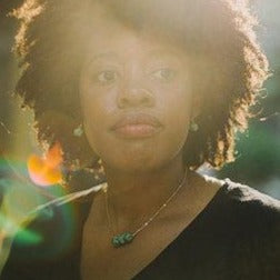 Woman with natural hair wearing a black top and turquoise necklace in sunlight, gentle lens flare effect.