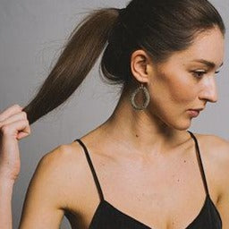 Woman in black top with ponytail and hoop earrings, neutral background, KTL